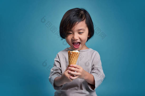 兴奋的亚洲小孩手里拿着美味的<strong>冰淇淋</strong>。工作室的空旷空间被<strong>彩色</strong>蓝色背景隔离。学校教育概念.