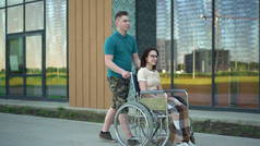 一个年轻的男人带着一个坐在轮椅上的年轻女人.一个助手载着一个残疾人坐在轮椅上沿街行走.残疾人特别交通.