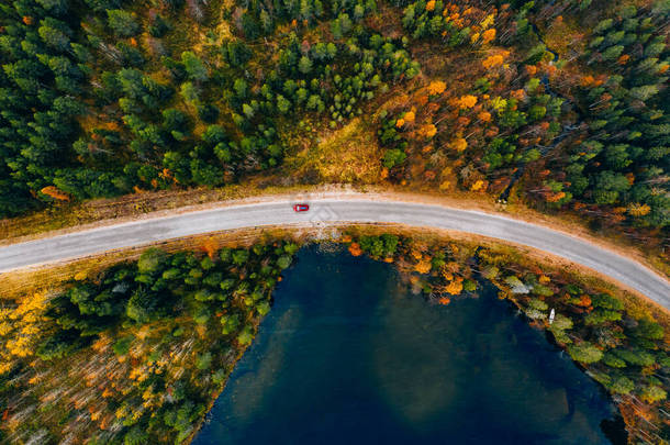 芬兰黄橙秋<strong>林</strong>蓝湖带红色轿车的农村公路空中景观.