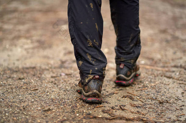 穿着<strong>湿透</strong>了的裤子和泥泞的靴子走在山路上的远足者的腿