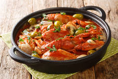 一锅鸡肉Marengo与小龙虾，蘑菇，橄榄，大蒜，西红柿和什锦在桌上的平底锅特写。横向a