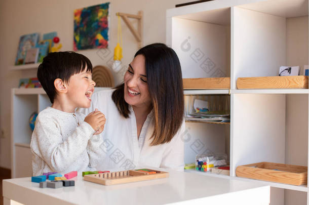 小不点小子在玩小提琴手的木头拼图和妈妈或老师的帮助。在家做家务。学习社区。Montessori Schoo