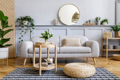 斯堪的纳维亚客厅内饰有设计灰色沙发、木制咖啡桌、热带植物、架子、镜子、家具、格子床、茶壶、书籍和精致的个人装饰.