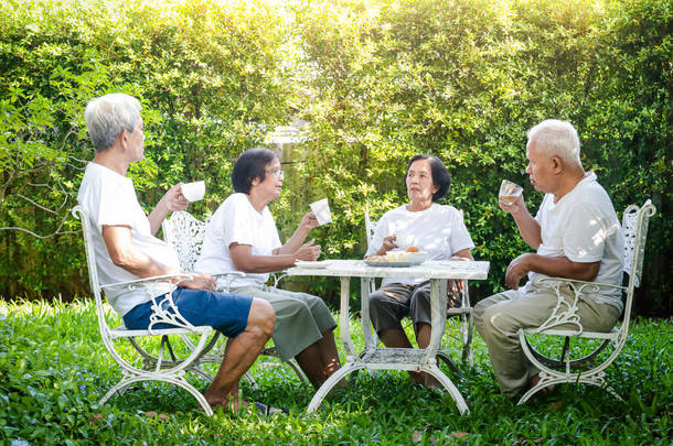 早上，亚洲老年人在屋前的花园里坐着，喝咖啡，聊天。高级社区、活动、保健的概念.