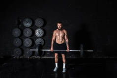 年轻的汗流浃背的强壮肌肉适合大肌肉的男人，他的肌肉保持着沉重的杠铃重量，并开始在健身房进行硬核交叉举重或举重训练