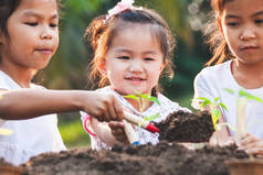 可爱的亚洲孩子们在黑土上种着幼树，一起在花园里玩乐