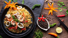 方便面与炒辣海鲜和各种调味品在黑色石板上的顶部与木制桌面，垃圾食品和亚洲餐的概念