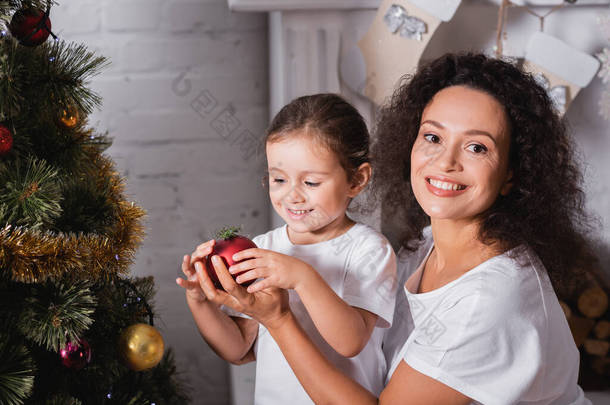 母亲和女儿带着圣诞舞会来到家里的圣诞树旁
