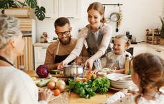 积极的年轻家庭主妇，带着小女儿，丈夫和祖母围坐在厨房桌子旁，准备美味的健康食品，并配上新鲜的配料，供全家在晚饭时享用