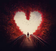 遵循你的心脏概念。一个孤独的人迷失在秋天的森林里，找到了走出森林的路，穿过了心形的树木。超现实和神奇的场景，红色秋天的色彩.