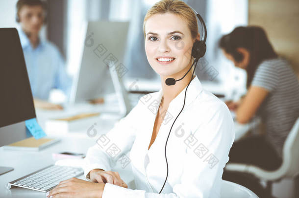 金发女商人使用耳机与客户服务办公室的人进行交流和咨询。呼叫中心工作中的操作者群体