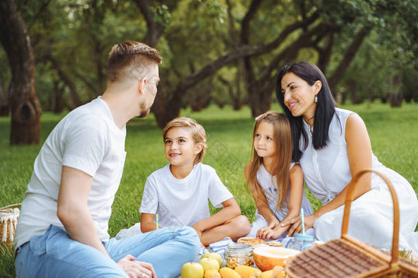 一个快乐的家庭，带着两个孩子在绿园野餐时在草坪上休息.