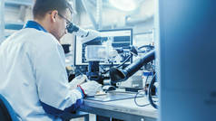 白色工作服中的电子工厂工人正在通过数字显微镜焊接一个印刷电路板。高科技工厂设施.