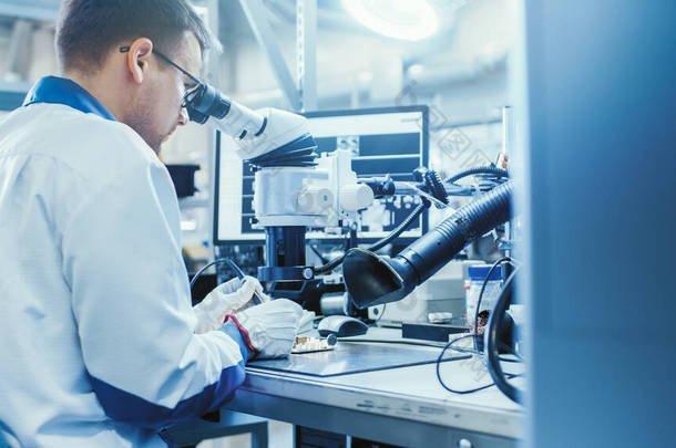 白色工作服中的电子工厂工人正在通过数字显微镜焊接一个印刷电路板。高科技工厂设施.