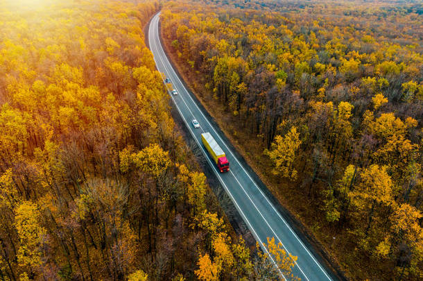 货物交付。日落了红色驾驶舱的白色卡车在柏油路上行驶，穿过秋天的森林。货物运输. 