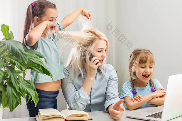 一<strong>位</strong>有<strong>两</strong>个孩子的年轻母亲在家里的电脑上工作。厌倦的生活方式家庭主妇自由自在。疲惫的母亲和<strong>两</strong>个小女儿