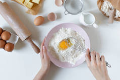 用配料和工具在白桌上烤面团.用搅拌器把面粉和鸡蛋放在碗里打.
