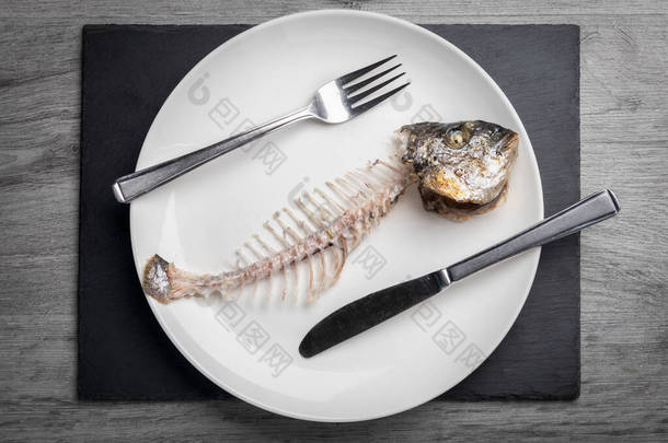 白盘上灰色木制桌子上的鱼骨被吃掉了.粮食<strong>短缺</strong>和苦难的概念.