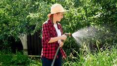 照片上，一个微笑的小女孩拿着水管浇灌后院花园的蔬菜。果园内有机蔬菜的种植与护理
