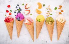 圆锥形蓝莓、开心果、杏仁、橙子和樱桃的各种冰淇淋口味，背景为白色石材。夏天和甜蜜菜单的概念.