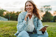 漂亮的快乐女人坐在绿地公园里笑着用手机