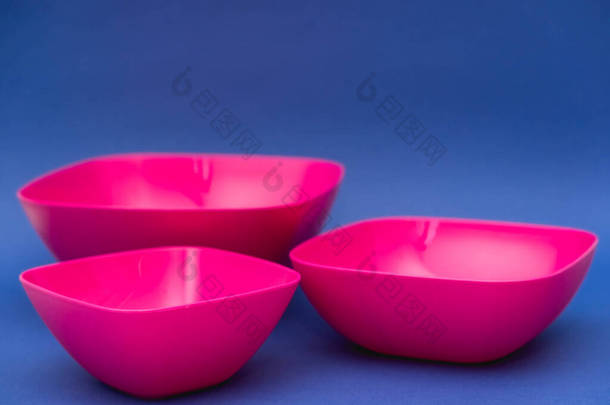 蓝色背景上的一组粉色盘子。厨房用的塑料器皿.顶部视图。<strong>简约</strong>主义风格。复制，空的<strong>文字</strong>空间.
