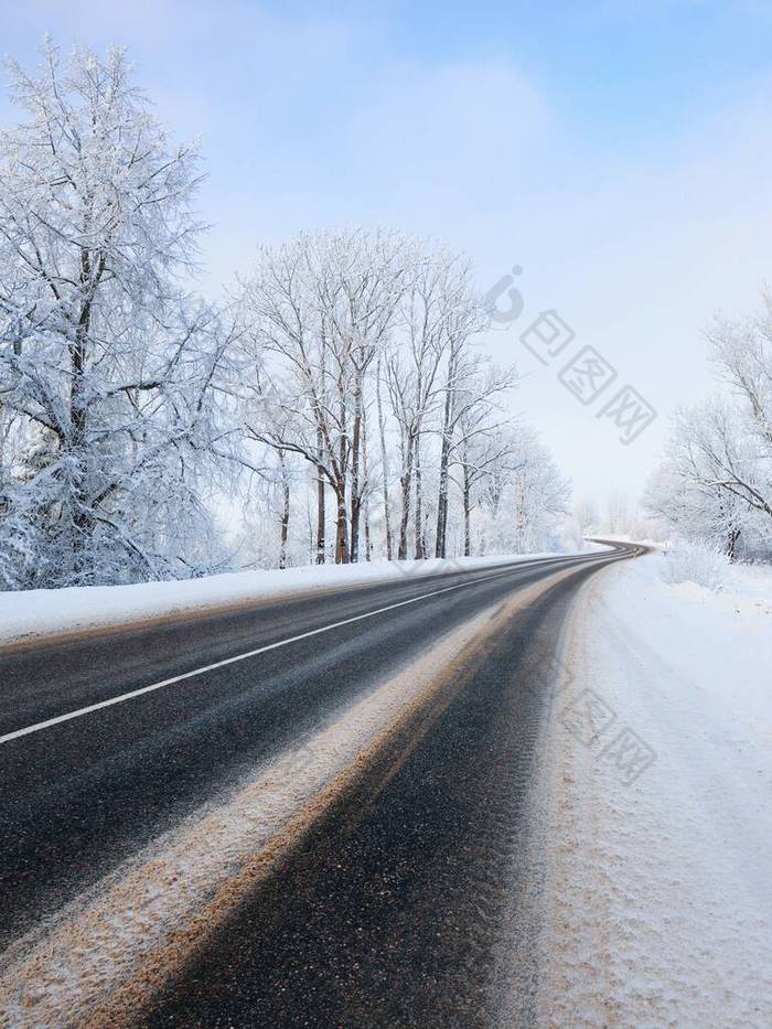 一个空旷蜿蜒的S形高速公路穿过雪地，森林，村庄的景象。冬季乡村风景。旅行、圣诞假期、后勤、危险驾驶、越野旅行、交通