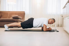 在轻便的阁楼内部的地板上锻炼的同时，让老年人自信地做着木板的姿势。做剧烈运动在家训练。人的训练要有合适的身体。晨练.