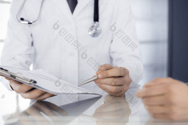 不为人知的男医生和女病人坐在诊所和使用剪贴板讨论当前的健康检查。医院的医疗服务很好医学概念