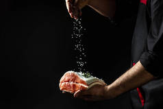 厨师把盐放在鲑鱼片上。将海盐撒在黑色冰冻的空气中。横幅,菜谱位置为文本.