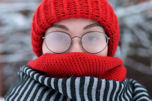 在寒冷的雪天，一个戴着迷蒙眼镜的年轻女子在户外的画像，相机放大了