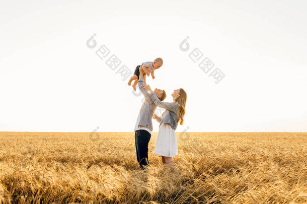 快乐的家庭在夏天散步，妈妈、爸爸和孩子在麦田里散步，欣赏美丽的大自然，夕阳西下