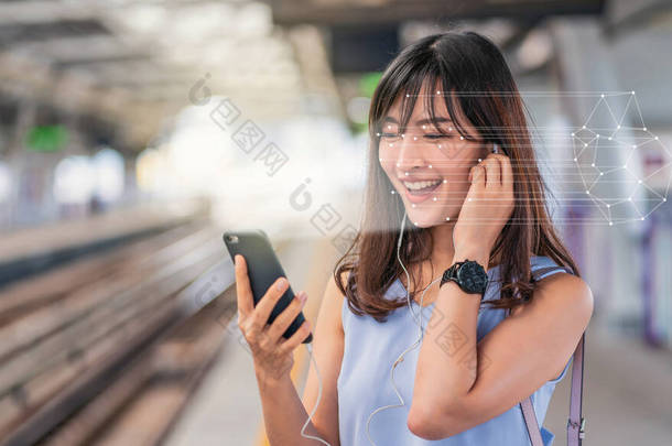 亚洲妇女通过智能手机进行面部识别，并在火车站平台上收听音乐、生物鉴别和<strong>人工智能</strong>概念