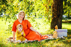 两个幸福家庭的画像。穿着橙色衣服的金发妈妈和女儿在公园里野餐.阳光.