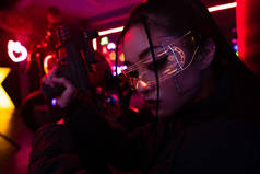 armed asian woman in sunglasses holding blurred gun outside 