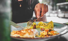 女人拿着叉子和刀把鸡胸肉和土豆放在盘子里吃 