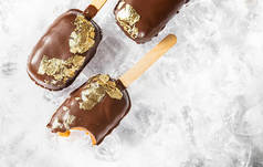 冰棒，上面覆盖着巧克力，顶部有一片可食用的金叶，背景冰封着雪。棒棒糖和甜甜的甜点在手杖上。顶部视图