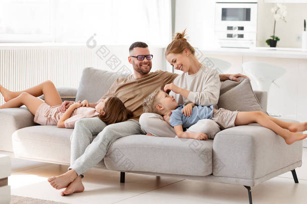 父母表达对孩子的爱。由四个人组成的美丽而快乐的家庭，父母和两个可爱的孩子一起呆在家里，在客厅的沙发上拥抱和放松