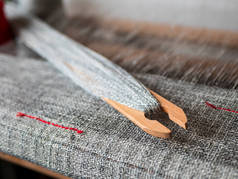 手织织布机上有带斑纹纱线的木制梭子.带红色条纹的梭织灰色织物