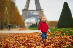 秋天的一天，穿着红色披风的可爱的小女孩在埃菲尔铁塔内散步。一个快乐的孩子在巴黎的街上玩得很开心。为儿童举办的户外秋季活动