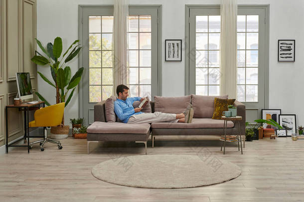 男人在看一本装饰客厅风格的书，灰色沙发工作台背景设计的书.