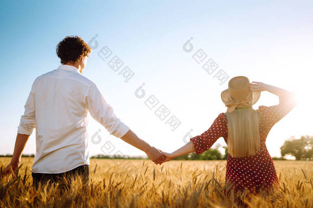 年轻快乐的夫妇拥抱在麦田上，夕阳西下。一起享受时光。青年、爱情和生活方式的概念.