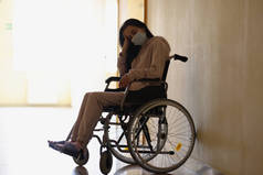 坐在医院走廊轮椅上戴防护口罩的年轻残疾妇女