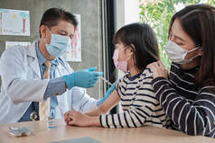 男医生，戴着口罩，为亚洲女孩接种疫苗，以预防考拉韦（COVID）19）在儿童医院的儿科诊所，母亲就在附近。注射治疗疾病，造成儿童疼痛.