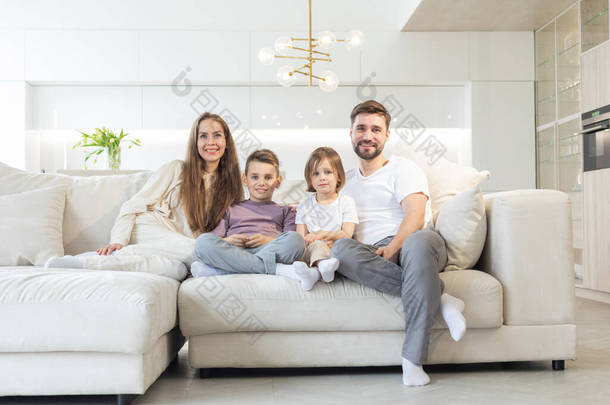 年轻父母和他们的两个孩子在家里的全家福，客厅的白色现代装饰