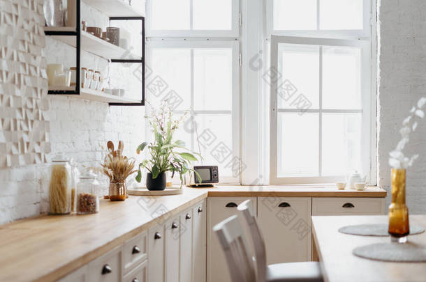 白色厨房的内部，配有木制现代家具。清理丑闻的鸟屋设计,<strong>台面台面</strong>明亮.桌上有玻璃厨具，房间里有复古装饰.