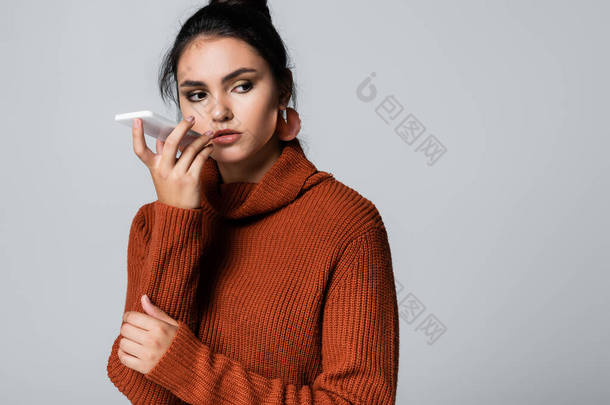 穿着针织毛衣的年轻女子用灰色隔离的智能手机记录语音信息