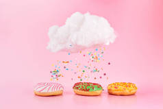 彩色水花从云中飘落.被分类的甜甜圈结霜，粉红色的釉面和洒在粉红色的背景上。各种装饰甜甜圈的概念新鲜美味的早餐.