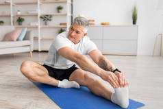 积极的生活方式。瘦小而成熟的男人伸展着她的腿，在客厅里练习瑜伽垫，复制空间