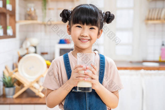 在家里厨房里拿着一杯牛奶的亚洲小孩的画像。幼稚园可爱的小女孩或女儿笑着呆在家里，开心地喝牛奶，然后看着相机.